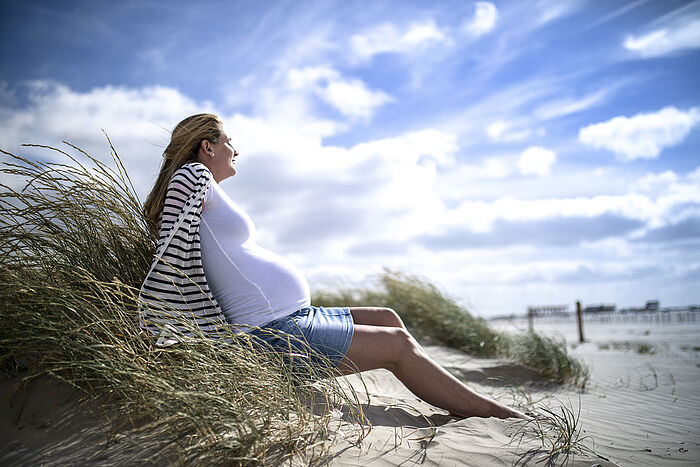 Das Bild zeigt eine schwangere Frau am Strand